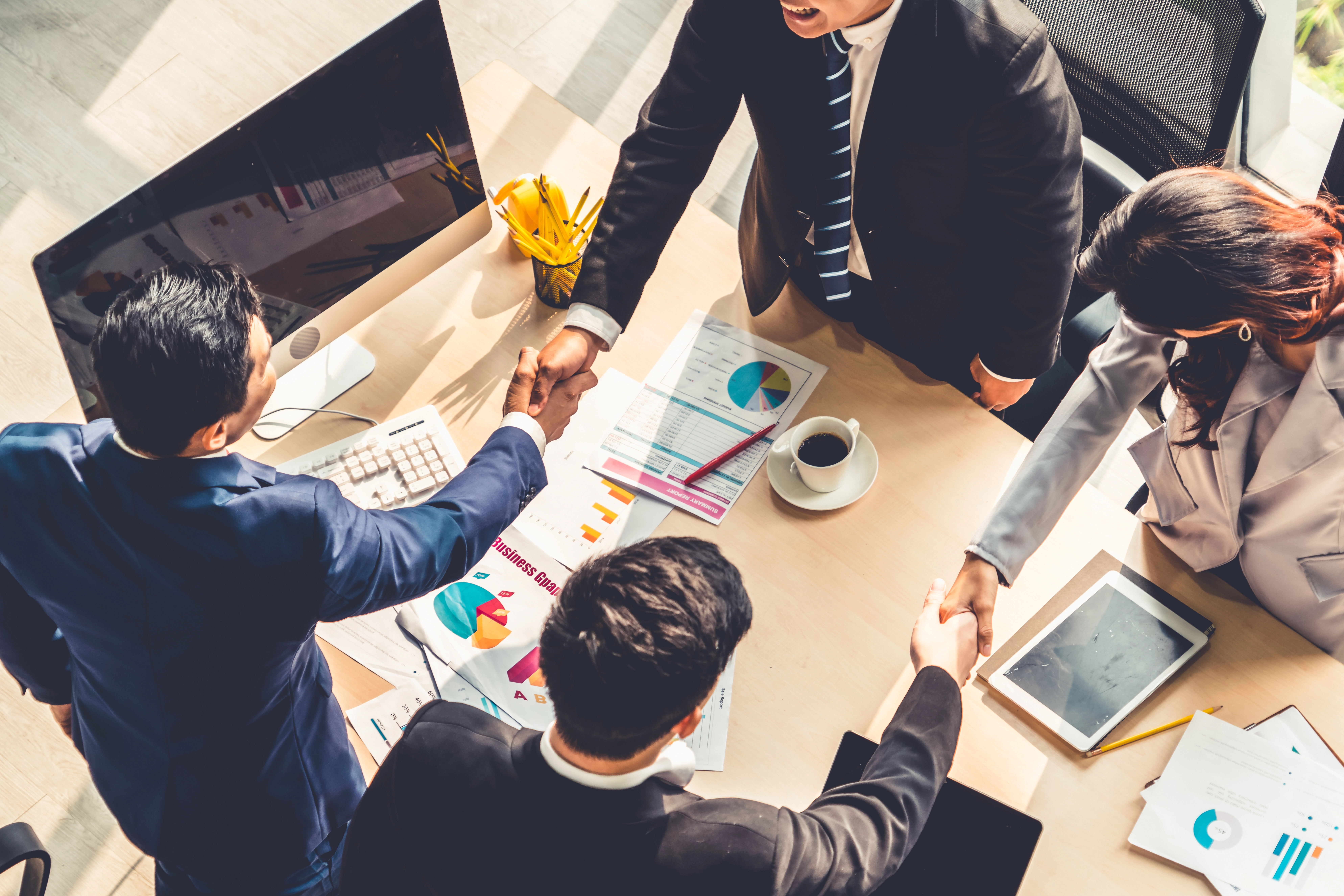 People shaking hands across a table covered in diagrams