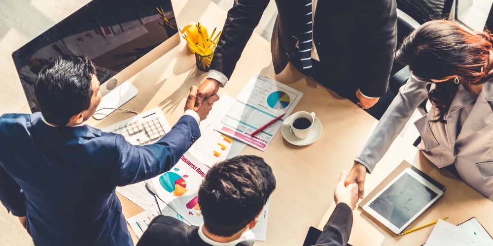 People shaking hands across a table covered in diagrams